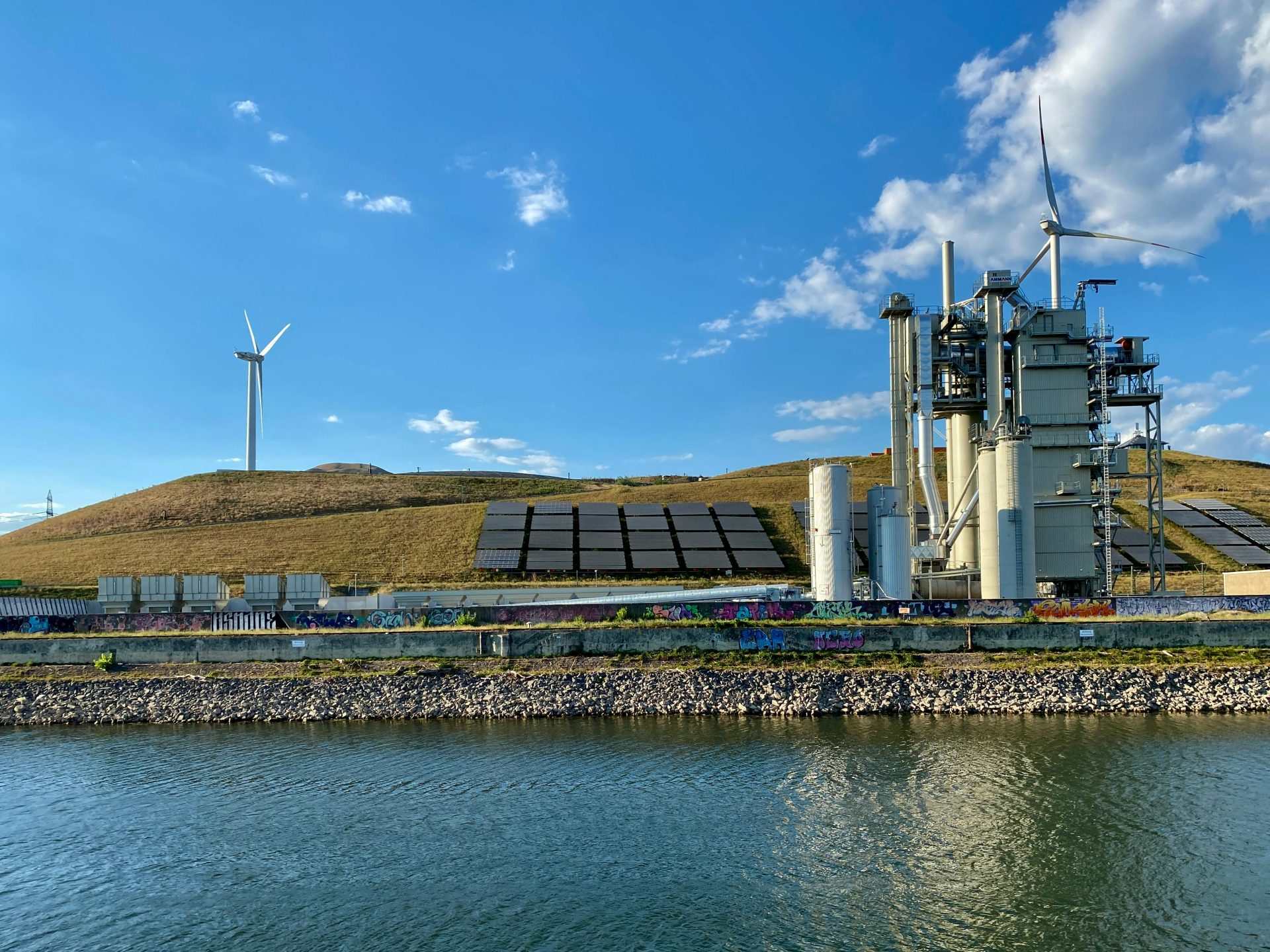 Instalación de energía renovable en Karlsruhe con turbinas eólicas y paneles solares junto a un río.